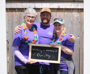 A group of three people, two women and a man, wearing purple t-shirts and holding a sign that says "Walking in memory of Dorothy"